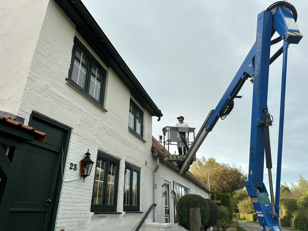 Schilder werkt vanuit een hoogwerker aan een woning